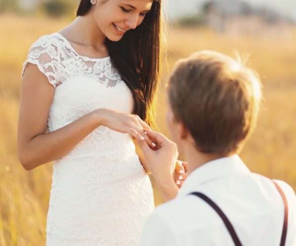 male-putting-engagement-ring-on-woman-hand-outdoors-in-a-golden.jpg